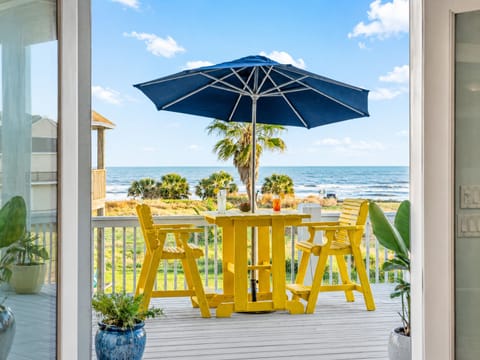 Galveston beach-view deck with yellow outdoor dining set, large umbrella, and Gulf views, perfect for morning coffee, coastal meals, and relaxing ocean breezes.