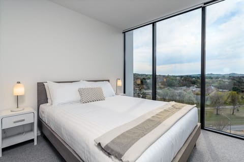Enjoy a queen-size bed with professionally laundered linens, large windows that fill the room with natural light, and a distant view of the National Arboretum, creating a bright and serene atmosphere.