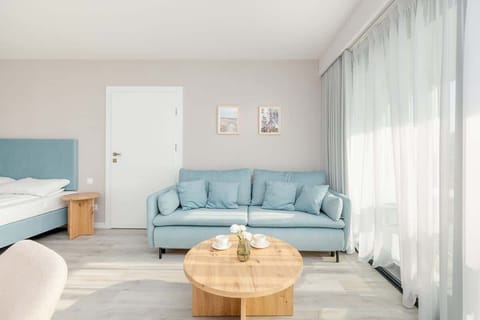 A cozy living room with a light blue sofa and sheer curtains letting in natural light. The perfect space to relax or unwind with a book or loved ones.