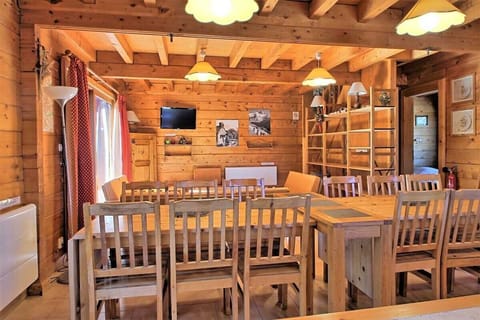 This spacious dining area features a large wooden table, perfect for gathering with loved ones.  The room is bathed in natural light from large windows and adorned with warm, wooden beams, creating a cozy and inviting atmosphere. The chalet's rustic charm