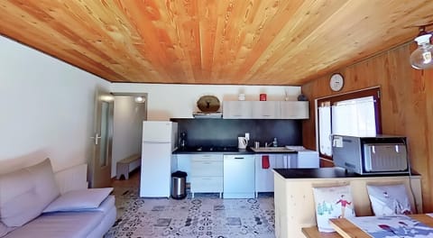 The modern kitchen is fully equipped with a dishwasher, microwave, fridge, and a four-burner stove. The wood-paneled ceiling adds a touch of rustic charm to the space, which also features a comfortable-looking sofa and a dining area with a large window. T