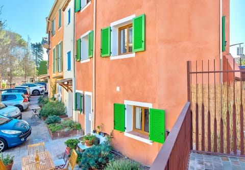 The exterior of the house features a charming terracotta facade with traditional green shutters, adding a touch of Provençal charm. The peaceful, cobblestone street in front of the house creates a picturesque setting, inviting guests to explore the quaint