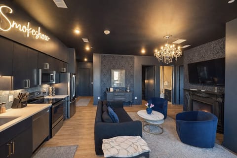 Enjoy a modern, open-plan living space with vibrant blue furniture, a dark blue sofa, and a stylish kitchen with stainless steel appliances and pendant lighting. A chandelier adds elegance to the cohesive design.