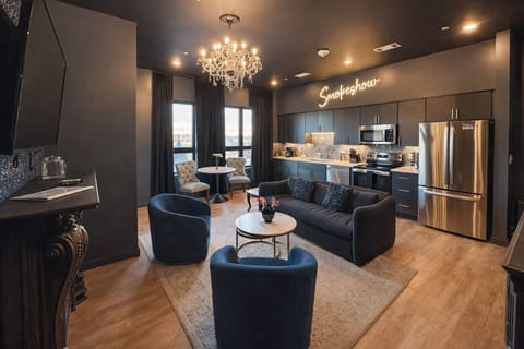 Enjoy a modern, open-plan living space with vibrant blue furniture, a dark blue sofa, and a stylish kitchen with stainless steel appliances and pendant lighting. A chandelier adds elegance to the cohesive design.