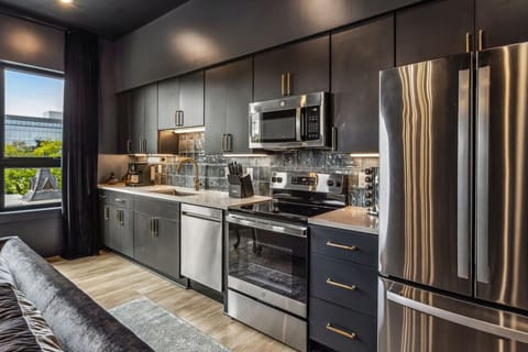 Enjoy a modern, open-plan living space with vibrant blue furniture, a dark blue sofa, and a stylish kitchen with stainless steel appliances and pendant lighting. A chandelier adds elegance to the cohesive design.