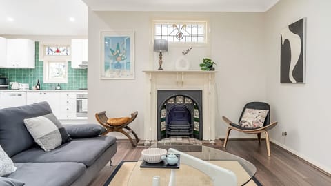 Mid-Century Hearth - An eclectic living room centered around an ornate vintage fireplace, featuring an iconic curved lounge chair, a glass coffee table, and a bright kitchen visible in the background.