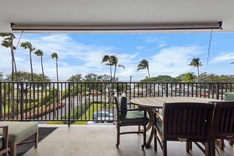 A covered lanai showcases tropical palm trees swaying in the breeze, overlooking lush green lawns and a peaceful neighborhood setting—ideal for morning coffee or sunset relaxation.