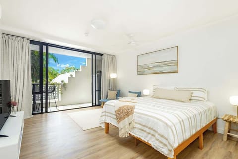 Soft natural light fills the open-plan studio, where a queen bed creates a comfortable retreat alongside calming neutral tones and direct access to the private balcony.