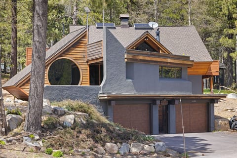 A striking mountain retreat blends modern design with natural wood elements, nestled among towering pines. The distinctive architecture features circular windows and a two-car garage, offering a unique alpine sanctuary.