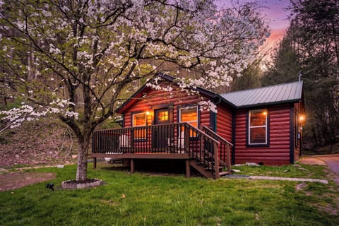 Charming log cabin surrounded by blooming spring trees, offering a peaceful retreat with warm glowing windows and scenic countryside setting.