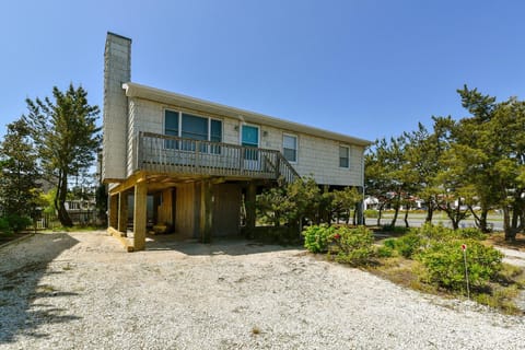 A coastal retreat nestled among towering pines and native greenery, offering a warm welcome with spacious ground-level parking and balcony views under clear blue skies.