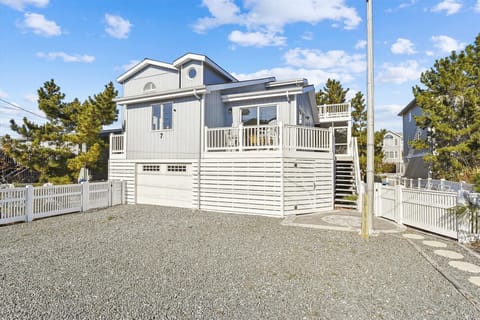 Beachside vacation home with classic coastal architecture, featuring multiple decks, spacious parking area, and surrounded by mature trees in a peaceful residential neighborhood.