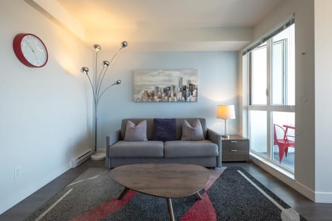 Welcome to your bright urban getaway! Relax in thi open-concept main living room featuring full-height exterior windows and comfortable sofa seating.