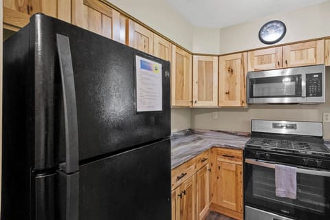 The Main House - Kitchen - Cozy kitchen with wooden cabinets, black appliances, and a wall-mounted clock, ideal for home chefs.