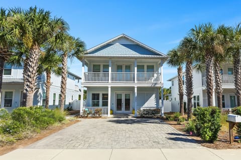 A charming two-story coastal home with traditional balconies and tropical palm trees, perfectly positioned in a peaceful beachside neighborhood.