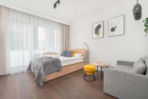 A stylish living room combining a bed and seating area, lit by floor-to-ceiling sheer curtains.

