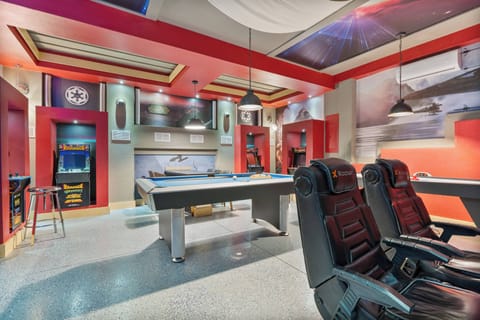 Discover our lively game room featuring a sleek pool table and energizing red walls. Unwind in comfortable black seating while enjoying the modern lighting, creating a unique atmosphere for your fun-filled retreat.