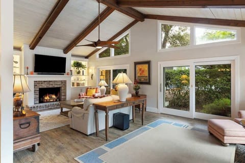 Spacious living room with vaulted ceilings, a fireplace, and large windows overlooking greenery.