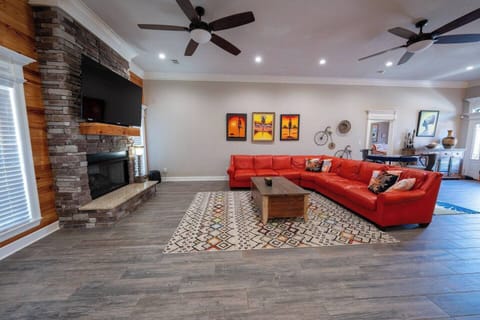The living room is an inviting, open-concept space that blends modern design with comfort. It features a large red sectional sofa as the centerpiece, offering plenty of seating for relaxation or entertaining. The warm wood accents, a sleek fireplace, and bright, bold artwork add vibrant touches, making this room both cozy and stylish. The room's spaciousness and contemporary de...