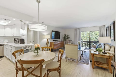 Polished wood tones and soft cream upholstery anchor this open living area, where natural brightness pours through the glass doors. A smooth stone breakfast bar flows into a cozy dining nook, creating a seamless space for slow mornings.