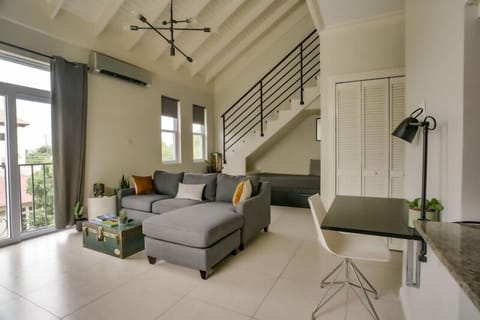 Bright living area w/ vaulted ceiling, staircase loft & comfy sofa beside tall windows