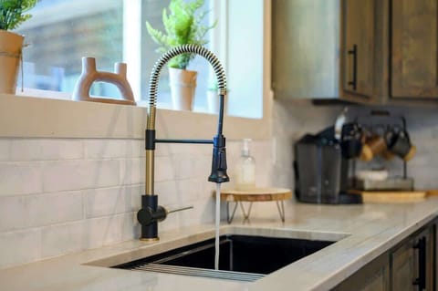 Modern farmhouse kitchen faucet with spring pull-down sprayer and potted plants on a quartz counter.