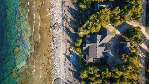 A stunning aerial view of a lakeside property, showcasing its prime location along a rocky shoreline with crystal-clear waters, surrounded by lush trees—perfect for a secluded getaway.
