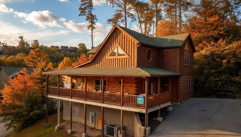 Rustic log cabin with wraparound porch surrounded by autumn foliage