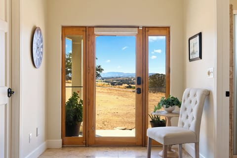 A bright and welcoming entryway, featuring a classic wood-framed glass door, a stylish tufted accent chair, and breathtaking panoramic views of the rolling hills.