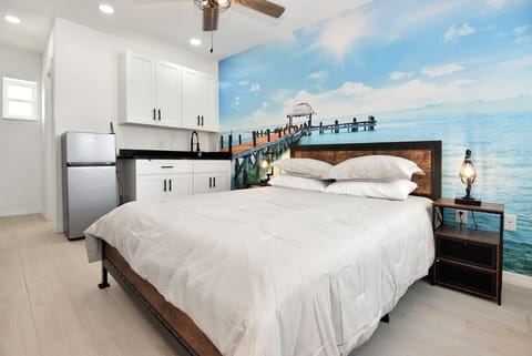 Queen bed with beautiful painting on wall next to kitchen