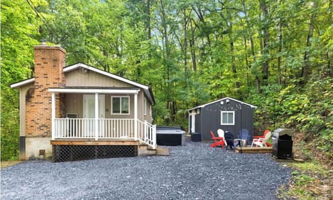 Cozy cabin with a porch, hot tub, and outdoor seating area surrounded by trees.
