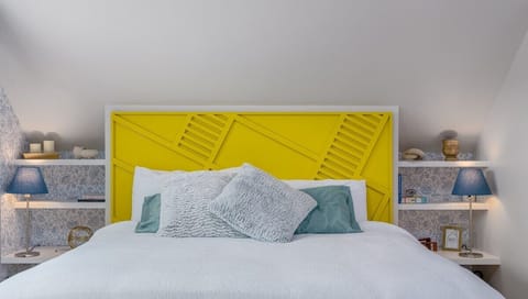 - Bold yellow headboard adds a playful pop of color to this bright and airy bedroom retreat
- Crisp white bedding and plush pillows create a cozy space to unwind and recharge
- Built in nightstands with patterned panels offer storage and style