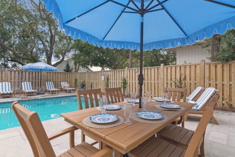 Dine al fresco at your poolside table, where elegant blue umbrella shade meets the sparkling water's edge for perfect outdoor entertaining.