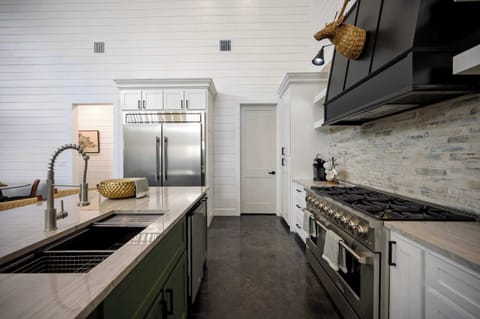 Spacious luxury kitchen with large stainless steel fridge, double oven, modern island sink, and rustic accents