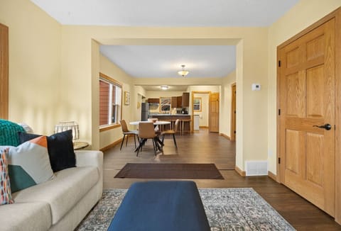 The living room features a comfortable sofa, seamlessly connected to an open-plan space with an island and chairs, alongside tables that offer a perfect blend of relaxation and dining areas.