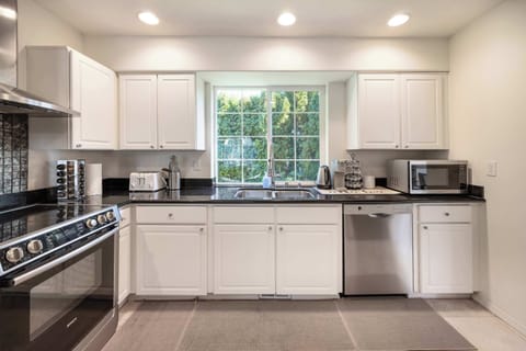 A bright, modern kitchen with sleek black countertops, stainless steel appliances, and large windows letting in plenty of natural light, perfect for preparing meals.