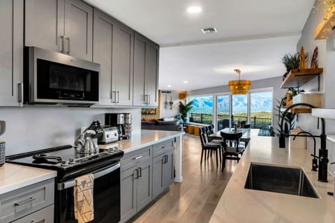 Chef’s kitchen with stainless appliances, island bar, and expansive dining table, designed for group meals and celebrations, complete with a full coffee station, complimentary snacks, and ample space for gathering.