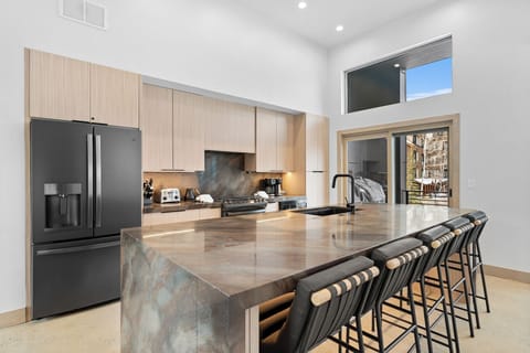 Full kitchen featuring stainless steel appliances, breakfast bar with seating for five, and balcony access.