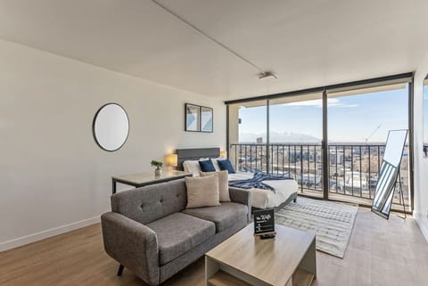 Modern studio with cozy seating, a plush bed, and floor-to-ceiling windows showcasing breathtaking city and mountain views 🌆🛋️⛰️