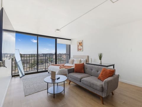 Bright studio with cozy bed, modern sofa, and floor-to-ceiling windows opening to balcony views 🌇🛋️