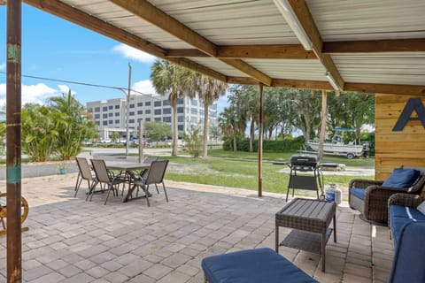 Covered patio with outdoor seating and grill overlooking a green lawn and nearby boat.