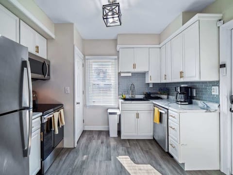 - Bright kitchen with stainless steel appliances and storage   - White cabinets and marble-look counters create modern style   - Functional layout with coffee maker and cooking essentials 
