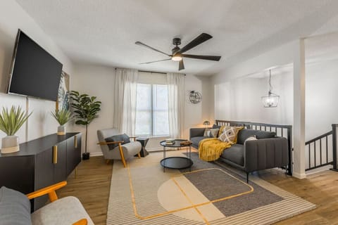 Bright and modern living area featuring stylish mid-century furniture, a large cozy sectional, and thoughtful decor accents. The space includes a flat-screen TV, lush greenery, and warm lighting, perfect for relaxing or entertaining.