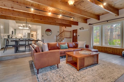 - Spacious living room with leather sectional and rustic wood beams  
- Large windows bring forest views and natural light indoors  
- Open layout connects cozy lounge to dining and kitchen