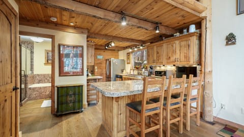 The cabin features a stylish granite bar table surrounded by high chairs, wooden cabinets, and up-to-date kitchen appliances. Bright glass windows create an airy feel, and a wall portrait adds an artistic flair.
