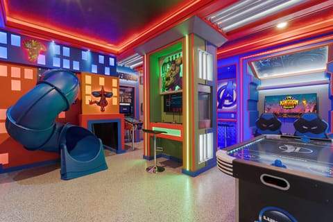 Step into a vibrant game room that promises endless fun, featuring a colorful slide and an air hockey table surrounded by dynamic wall art. The neon lighting adds an exhilarating touch, perfect for entertaining guests of all ages.