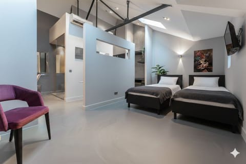 Modern, spacious room with two single beds, sleek gray floors, high ceilings, and a stylish partition wall in a bright, minimalist design.
