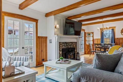 The cottage's character-rich living room features exposed beams, a stone fireplace, comfortable seating, and a television.