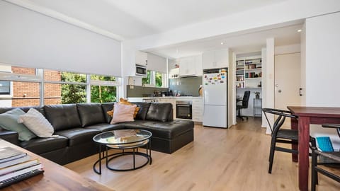 Relax in style within a bright living area featuring warm timber floors, a plush black leather corner sectional, and an seamless connection to the kitchen.