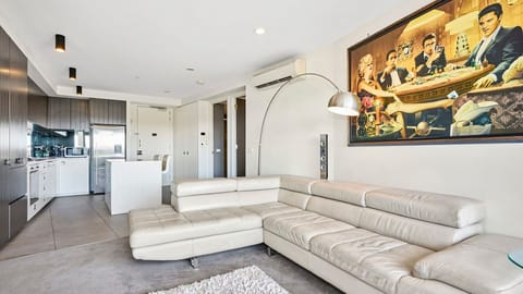 A bright, spacious living area featuring a sleek white leather sectional, contemporary artwork, and seamless flow into the kitchen.